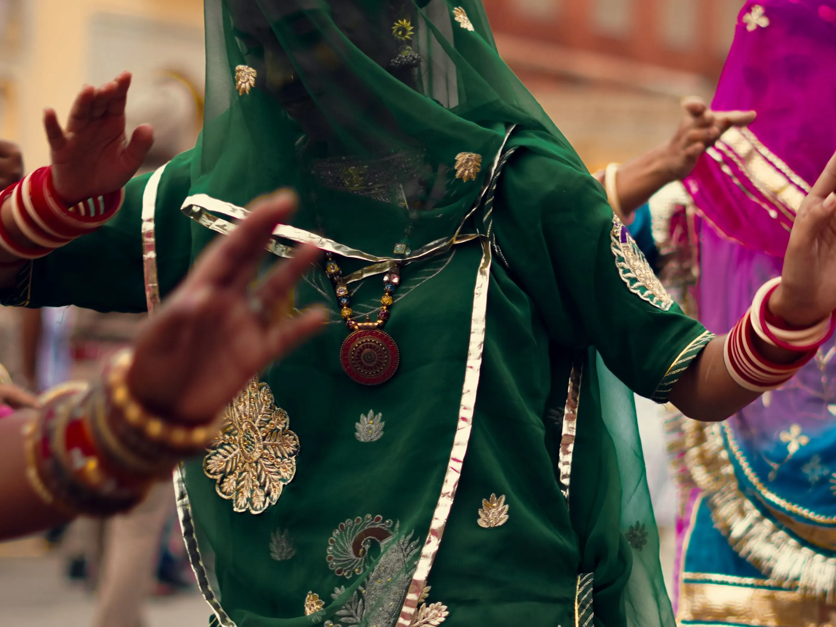 Stacked red bangles and a long pendant necklace over a green, embroidered poshak
