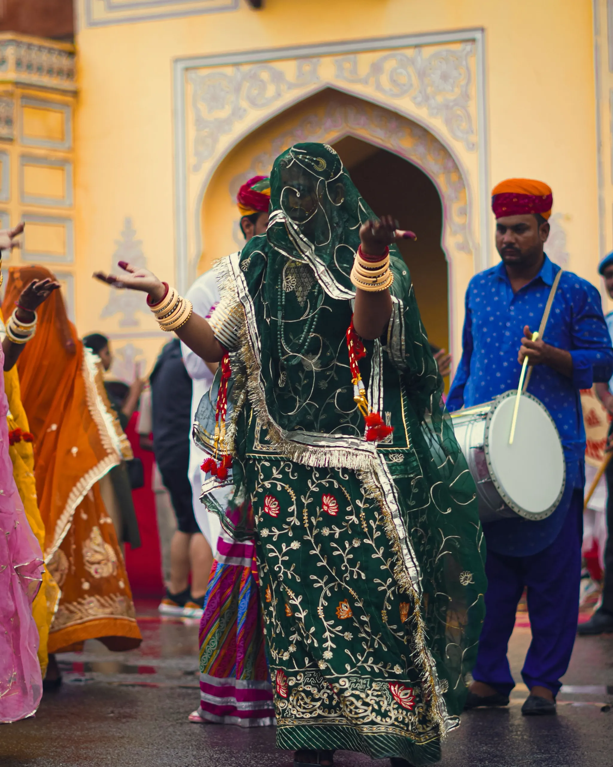A Ghoomar dancer in a green poshak, her odhani veiling her face, hands raised