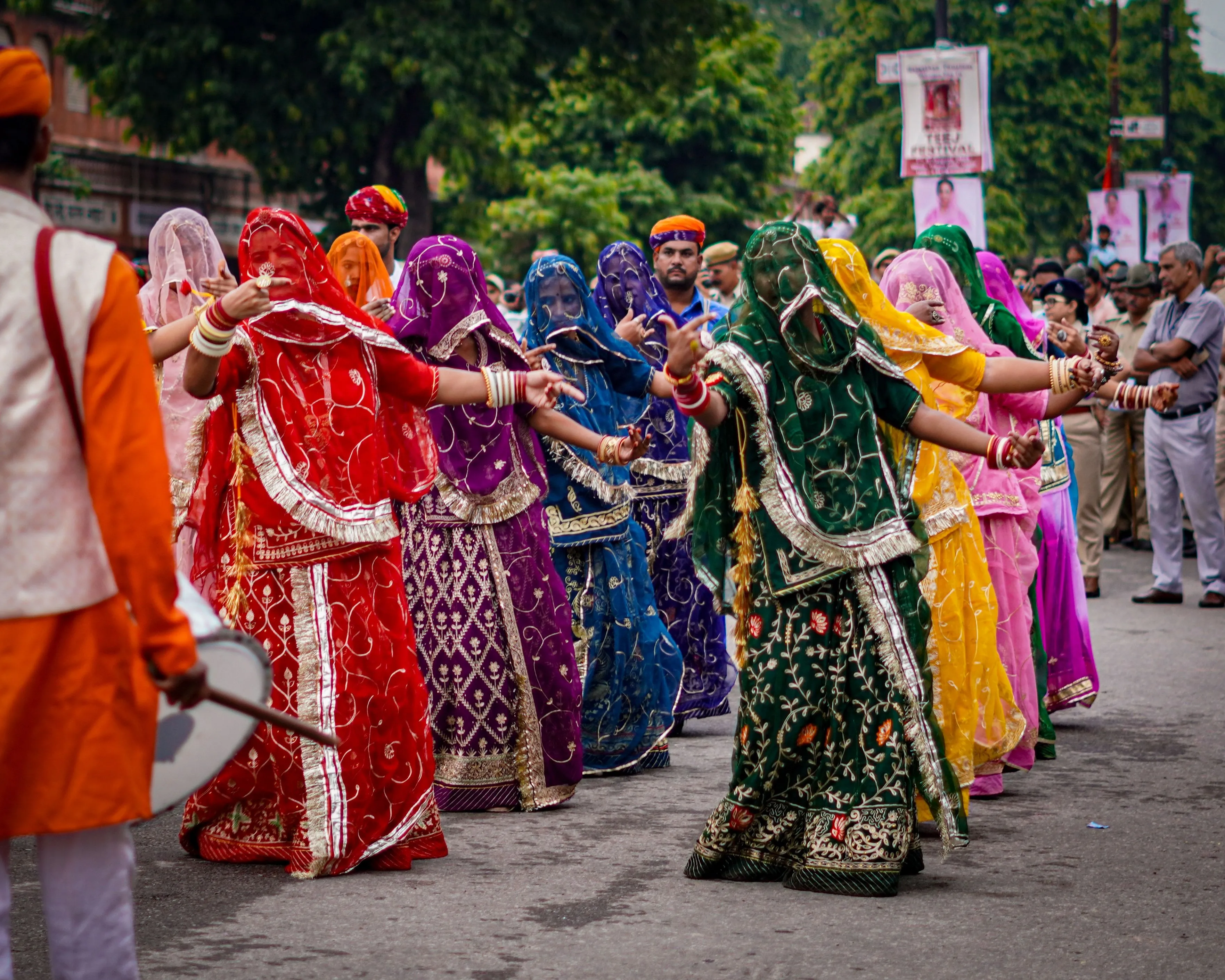 A line of veiled Ghoomar dancers in red, purple, blue, green and yellow poshak, arms outstretched