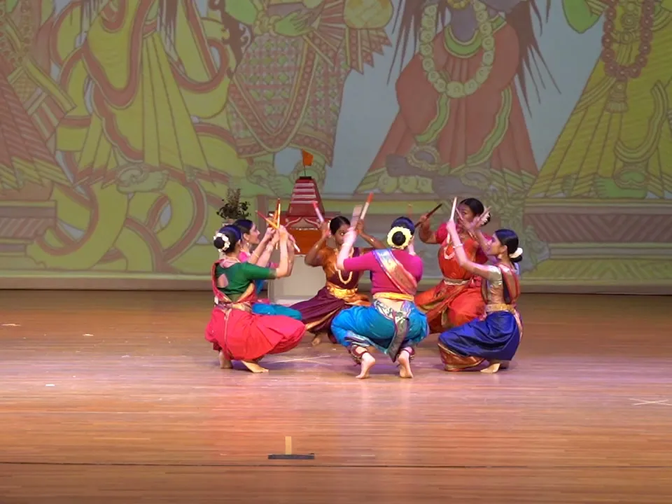 NSDA dancers crouched low in a ring, striking their sticks together