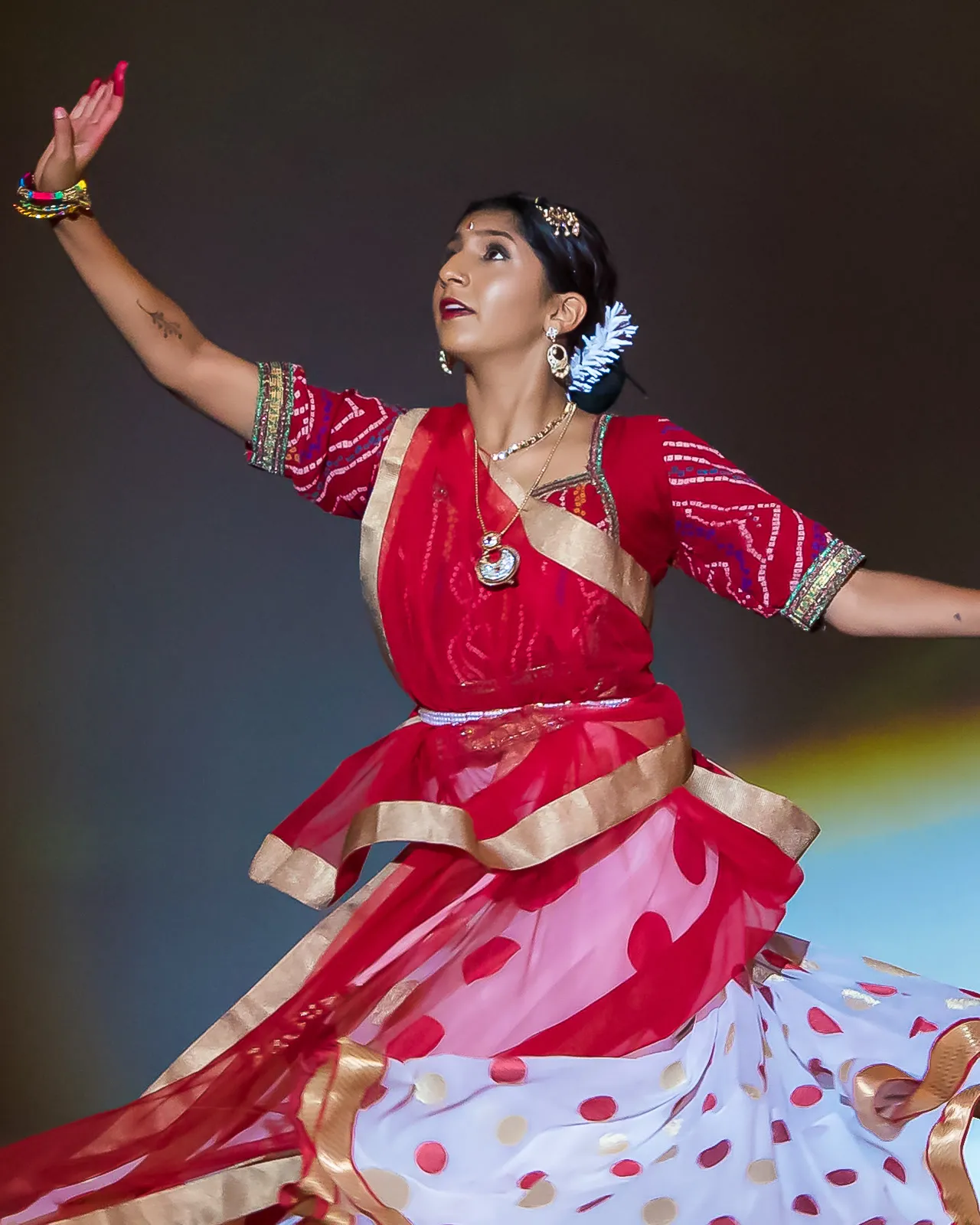 A senior Elite dancer in red and white, mid-twirl, arms outstretched