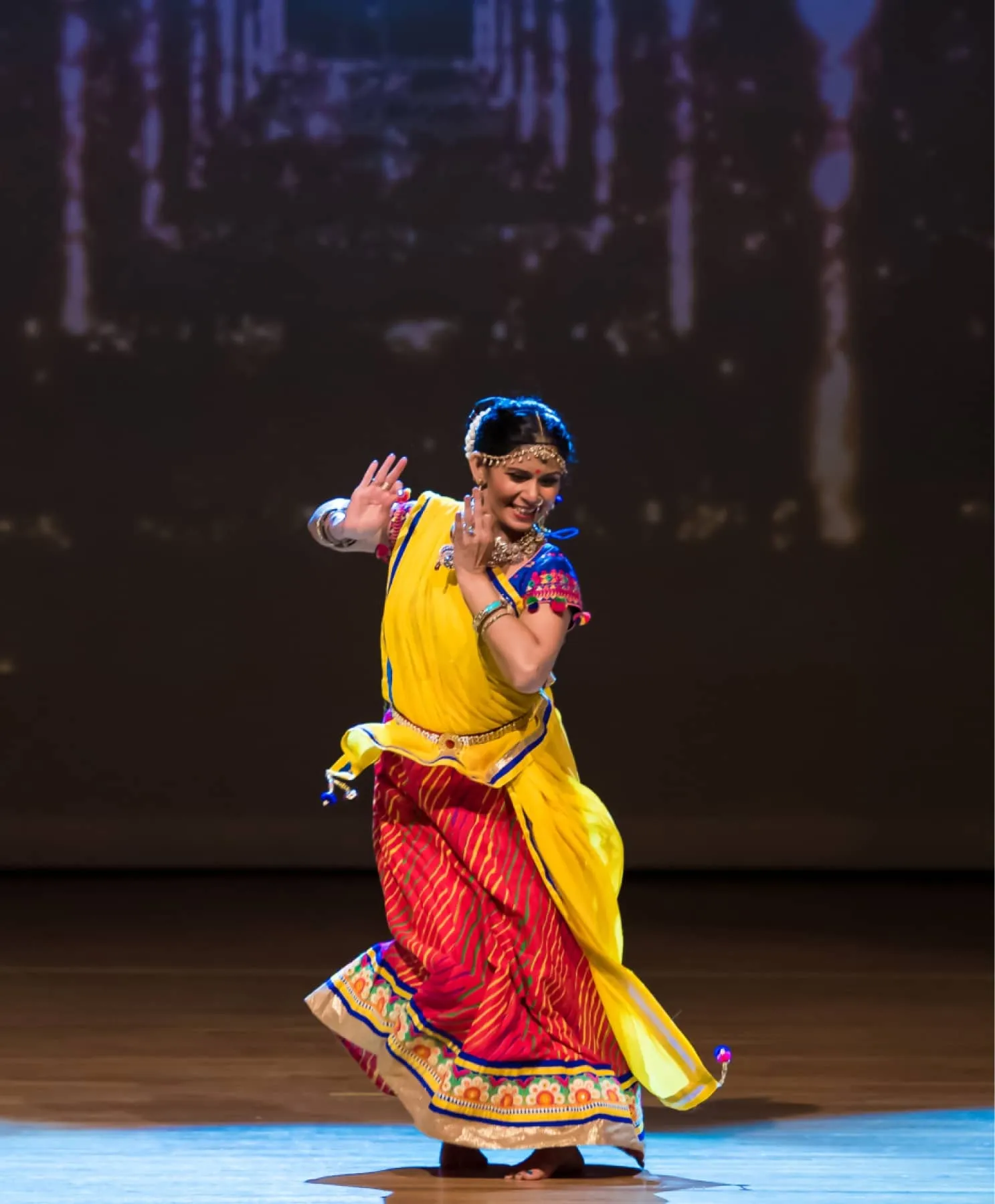 Vandita Parikh dancing on stage in a yellow and red folk costume