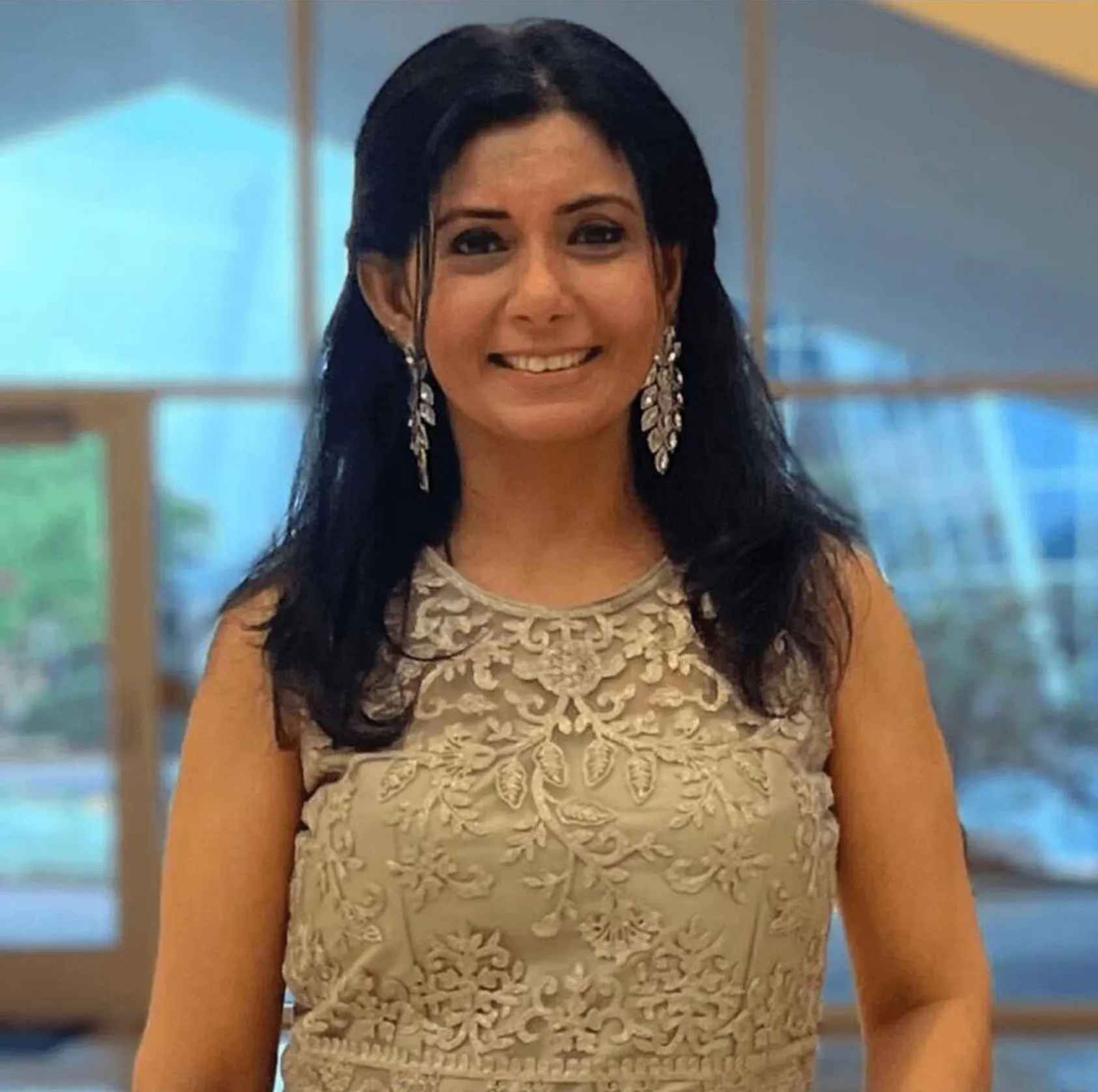 Vandita Parikh smiling, in a champagne lace top and silver leaf earrings
