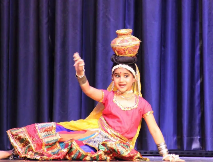 A young dancer balancing a pot on her head, reclining on stage