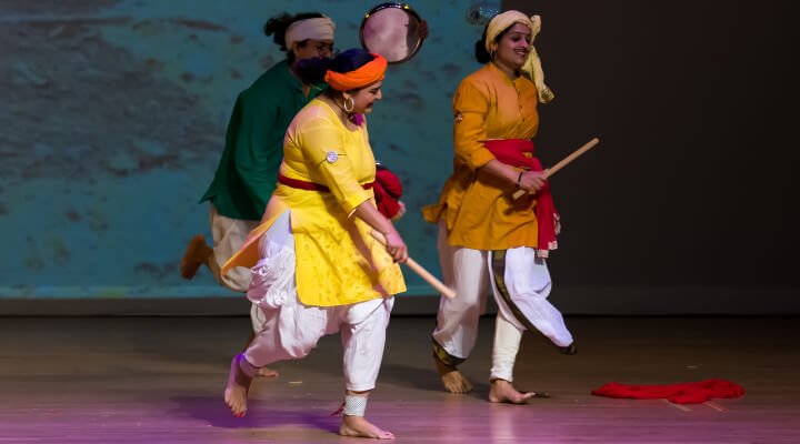 Students using plates and sticks as props on stage.
