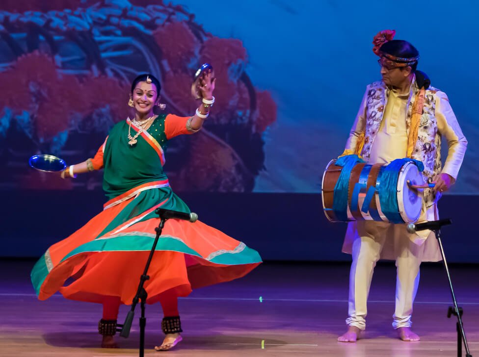 An NSDA student dancing around a person playing the dhol live on stage